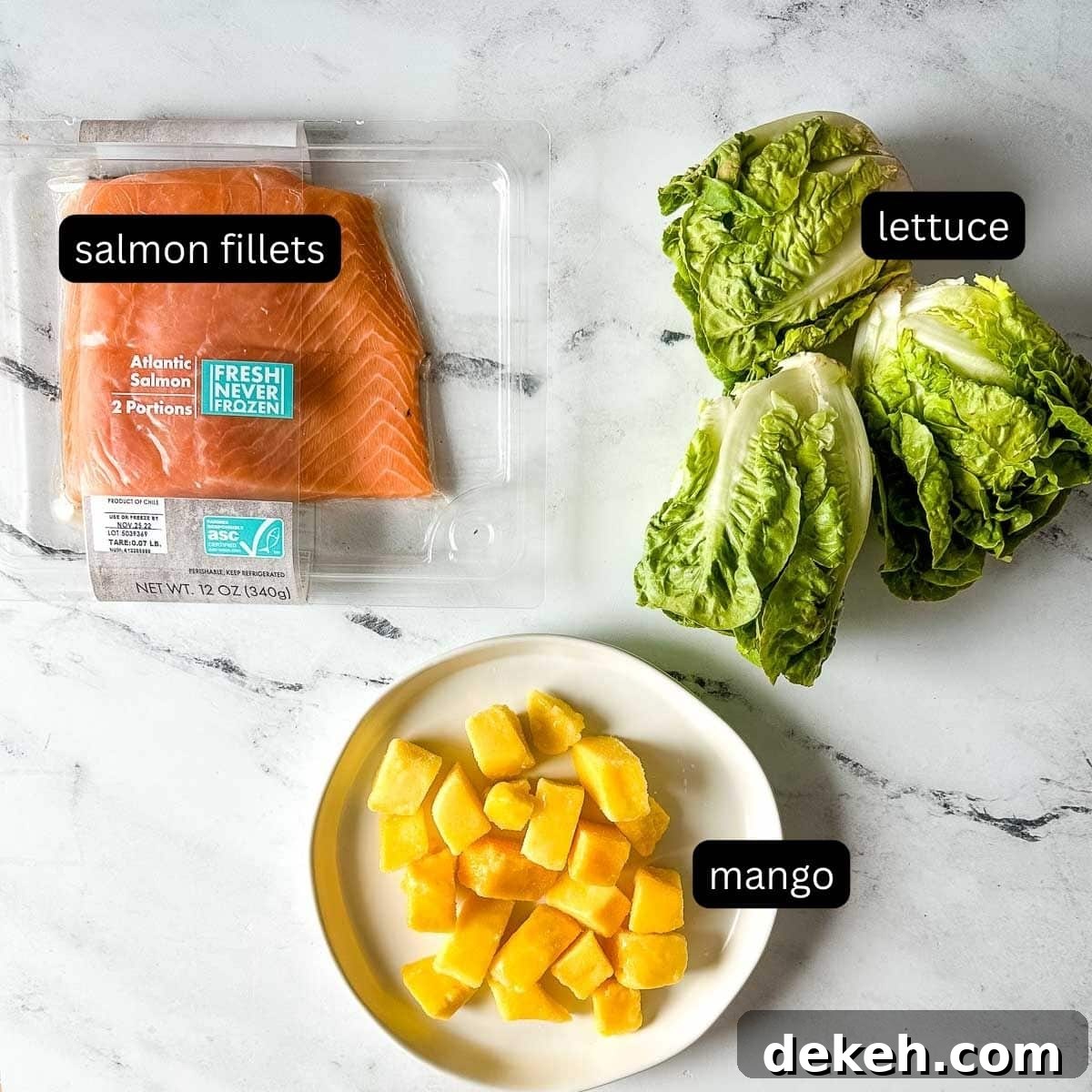 The labeled ingredients for mango salmon salad sit on a white marble counter.