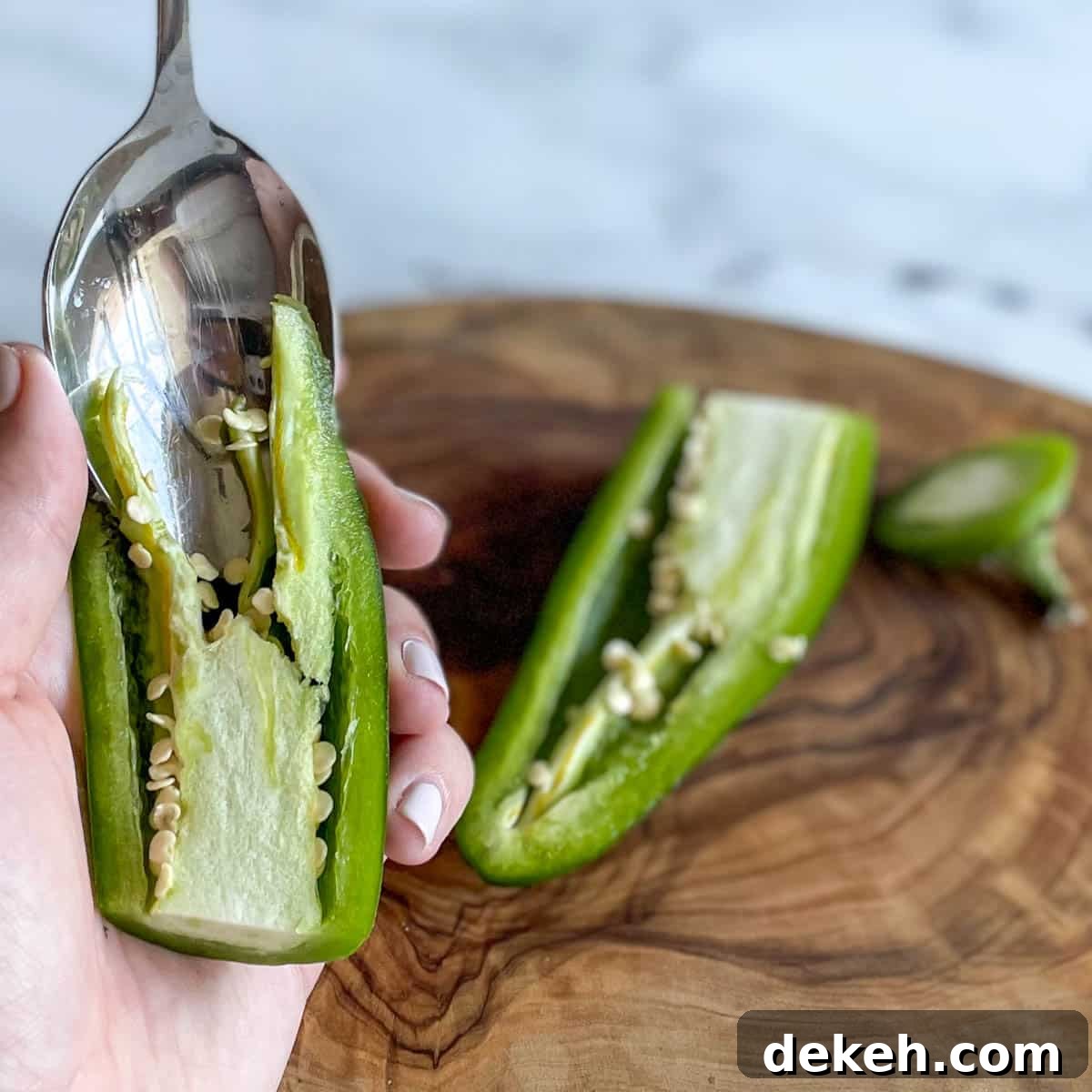 A silver spoon scoops out the membrane and seeds from a jalapeno.
