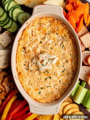 A large circular wood board with a hot crab dip in the middle with fresh produce, bread, chip and crackers around the dish.