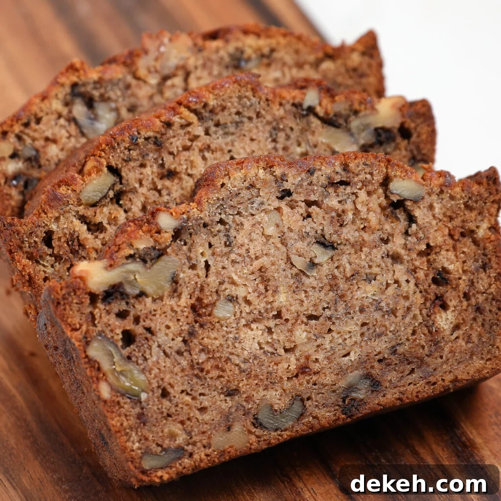 Three slices of moist Banana Bread with visible walnut pieces rest on a wooden cutting board.