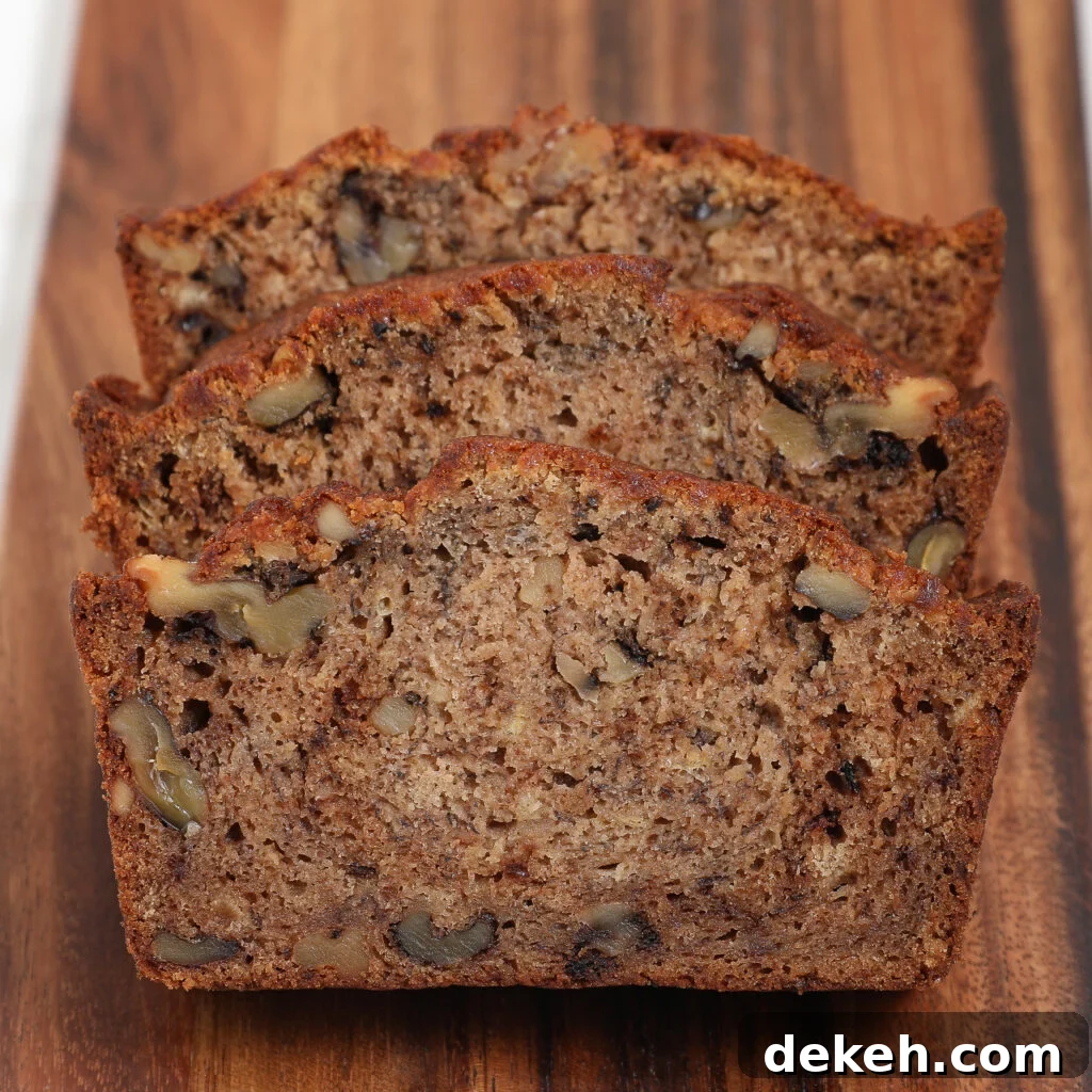 Three slices of Banana Bread with visible walnut pieces, arranged in a row on a wooden cutting board.
