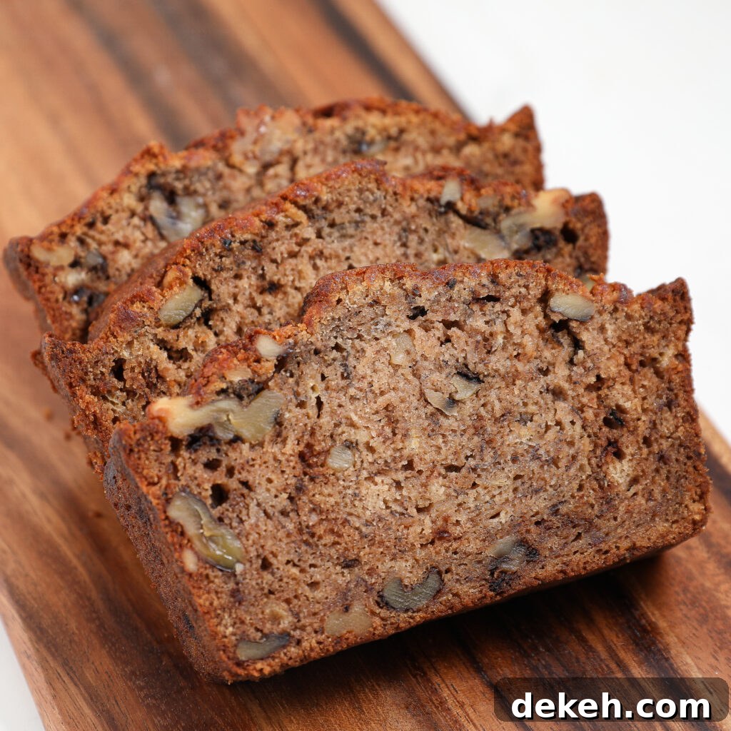 Three slices of classic Banana Bread with visible walnut pieces, arranged on a wooden serving board. The bread appears moist and dense with a golden-brown crust.