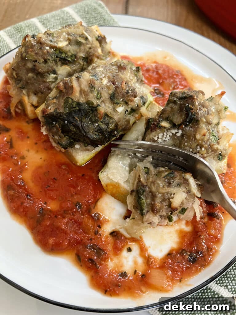Fork cutting into one piece of stuffed googootz squash over tomato sauce on a white plate.