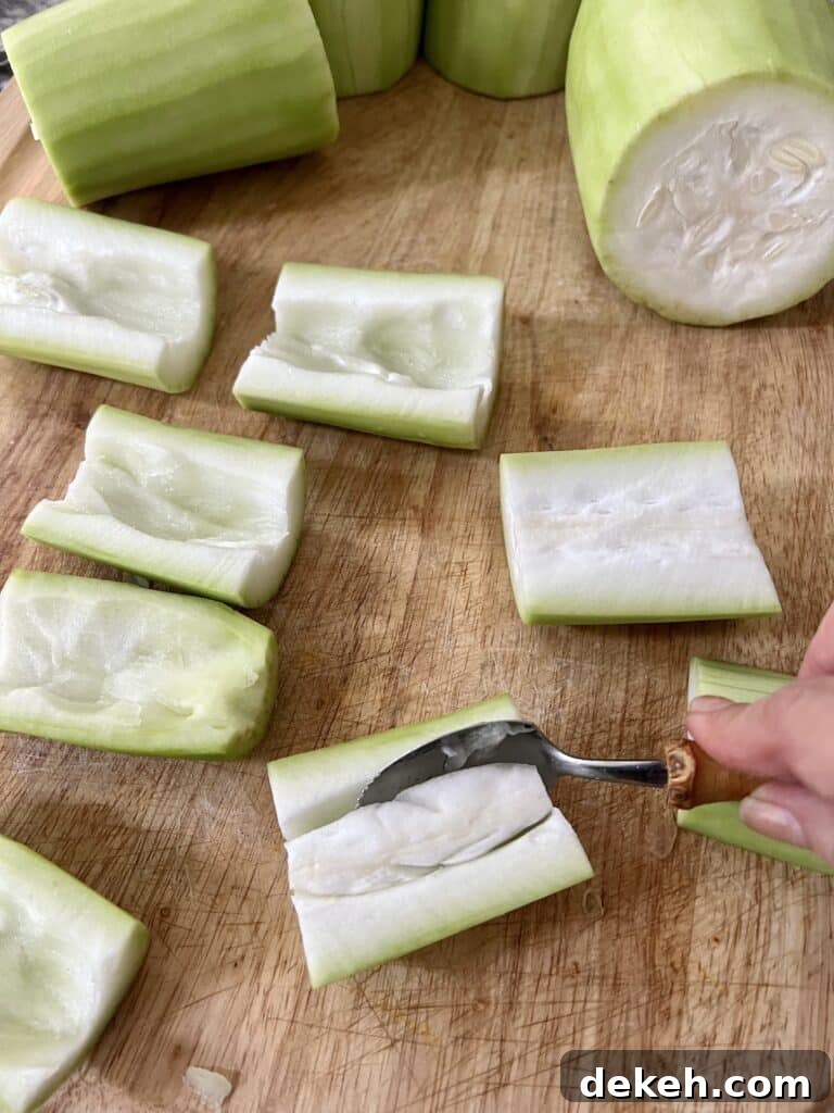 Using a grapefruit spoon to hollow out the pieces of cucuzza and also remove the seeds.