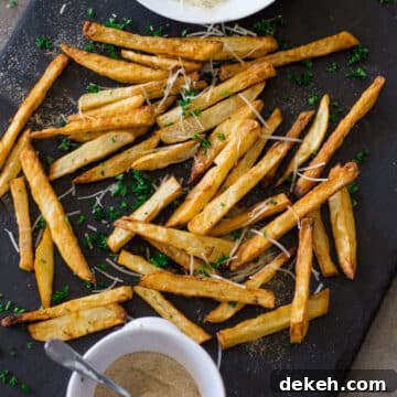 Cooked french fries on a black slate with parmesan cheese and seasoning