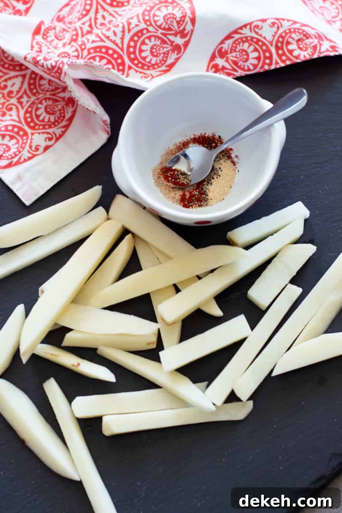 A cup full of seasonings for french fries, spoon in cup.
