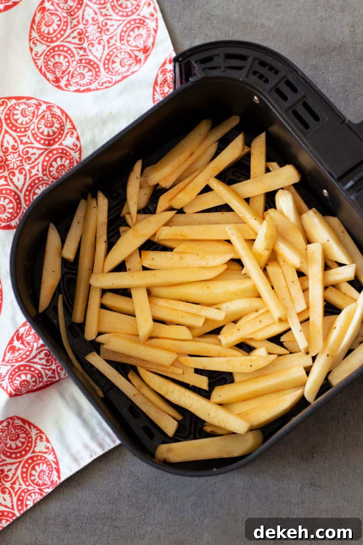 Air fryer pan filled with uncooked seasoned french fries.