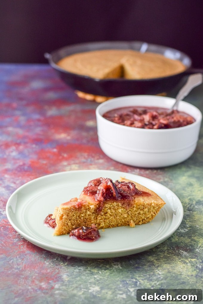 A red sauce draped over a slice of cornbread. There is a bowl of the sauce and a skillet of bread in the background