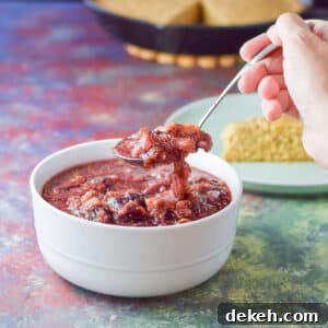 Spoonful of fig sauce held over a white bowl with cornbread in the background - Square