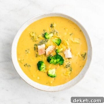 Vegan broccoli cheddar soup in a bowl garnished with bread and vegan cheddar cheese.