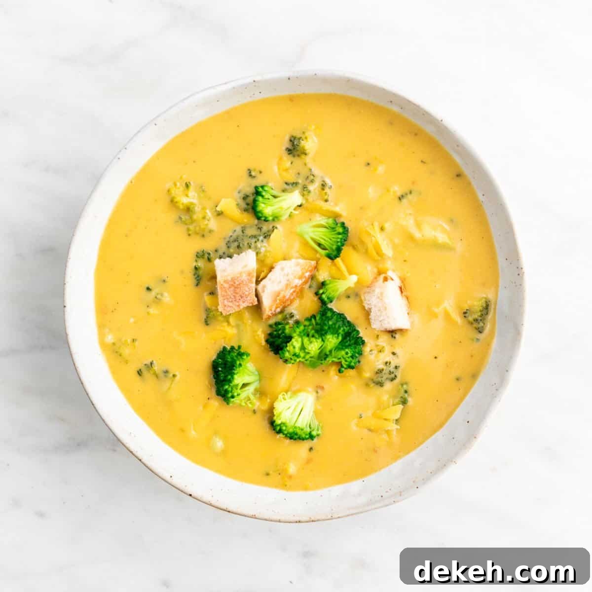 Vegan broccoli cheddar soup in a bowl garnished with bread and vegan cheddar cheese.