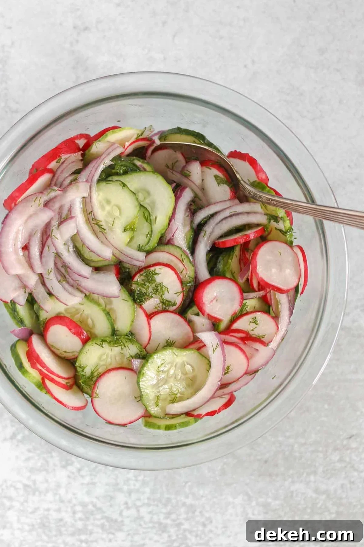 Cucumber, radish, and red onion being mixed in a glass mixing bowl.