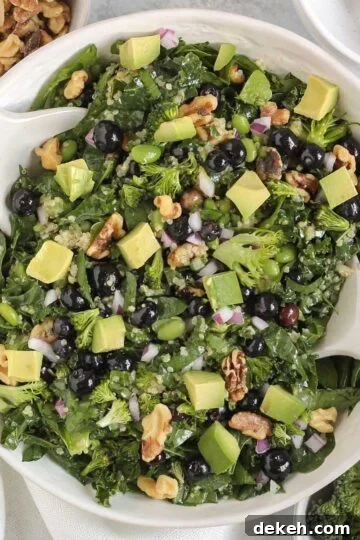 Superfood salad with blueberries, broccoli, walnuts, and avocado in a white serving bowl with white salad utensils.