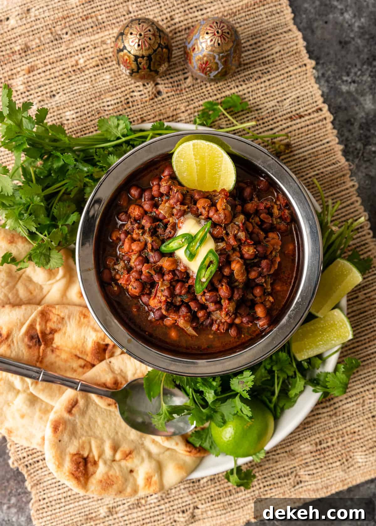 overhead: bowl of instant pot kala chana surrounded by fresh cilantro, lime wedges and naan flatbread