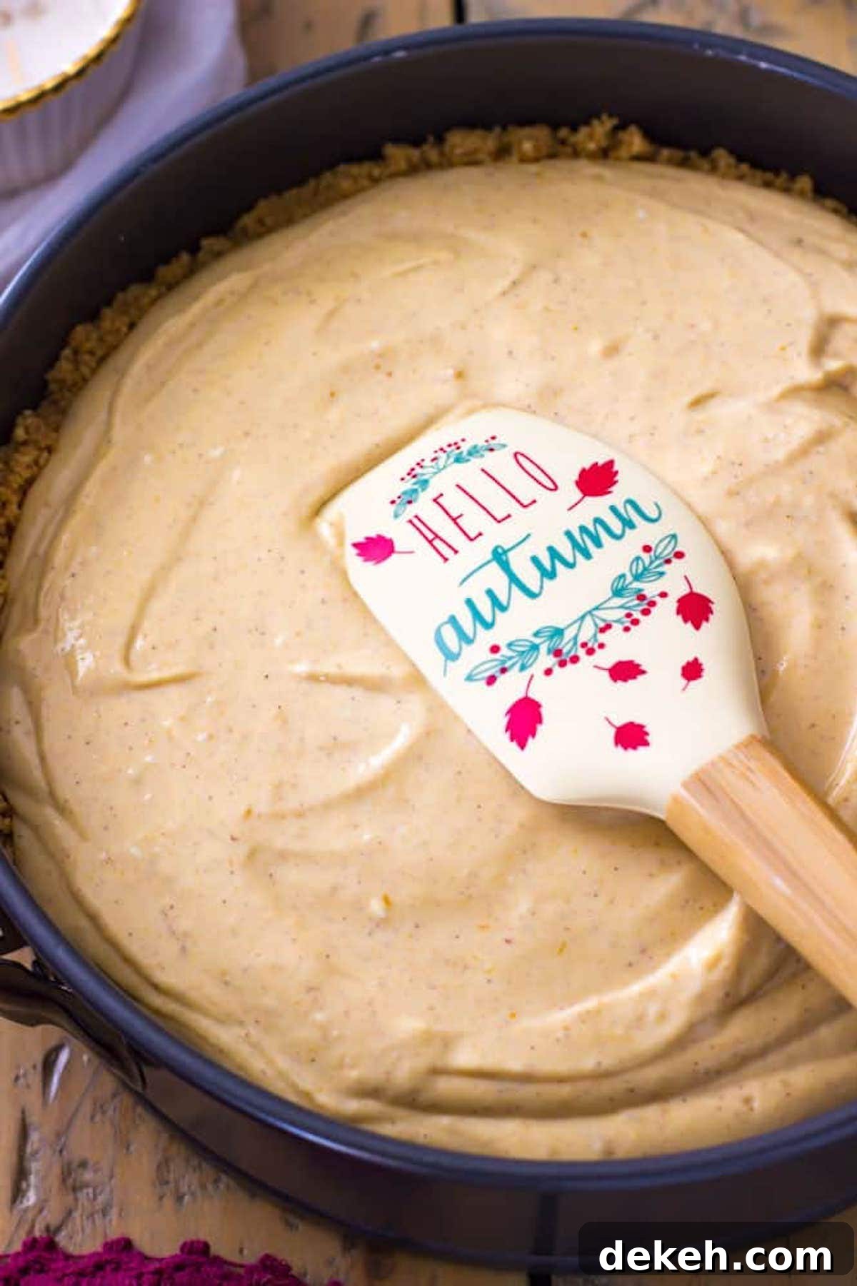 Fall-themed spatula smoothing cheesecake batter after being poured into a springform pan.