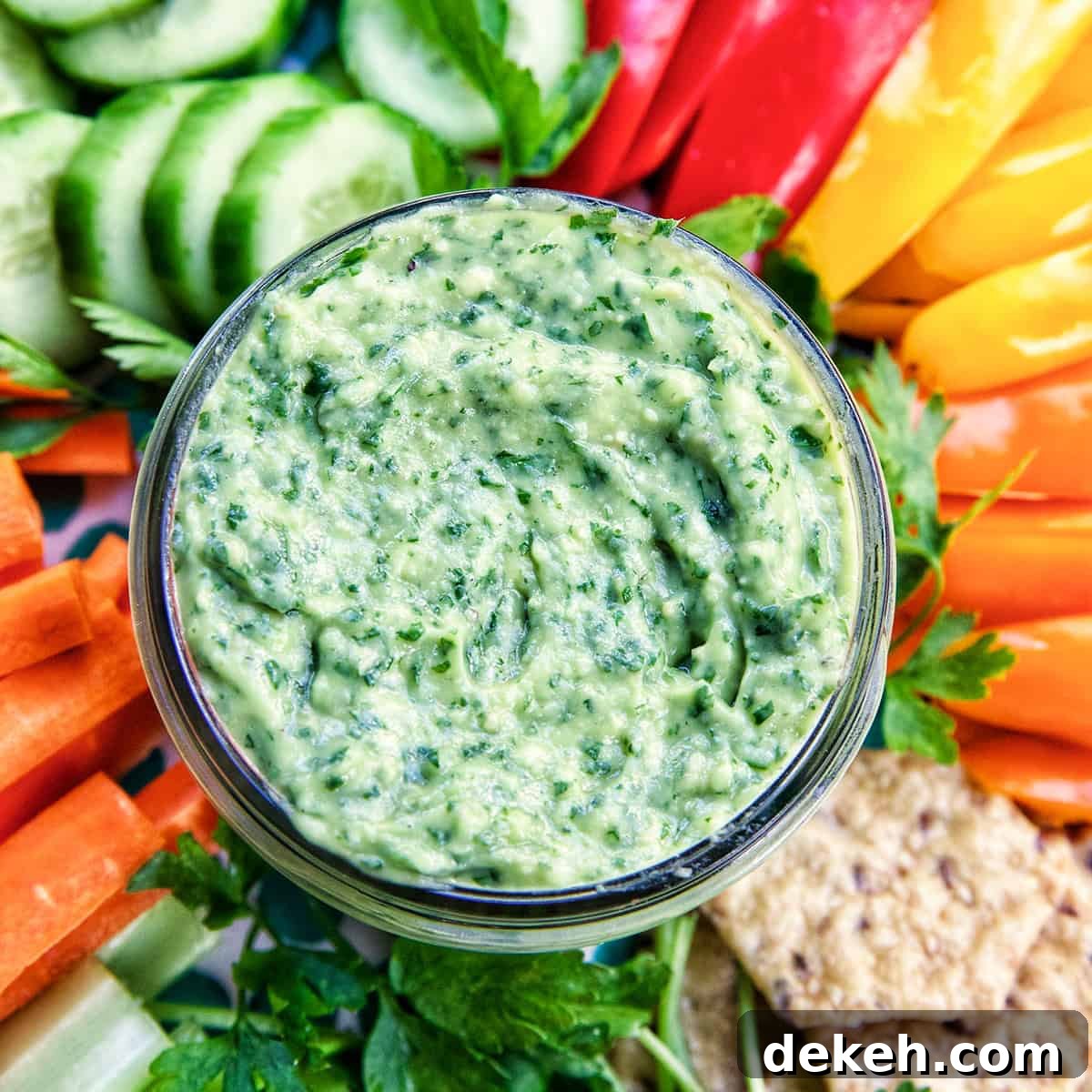 jar of vegan green goddess dressing in the center of sliced vegetables.