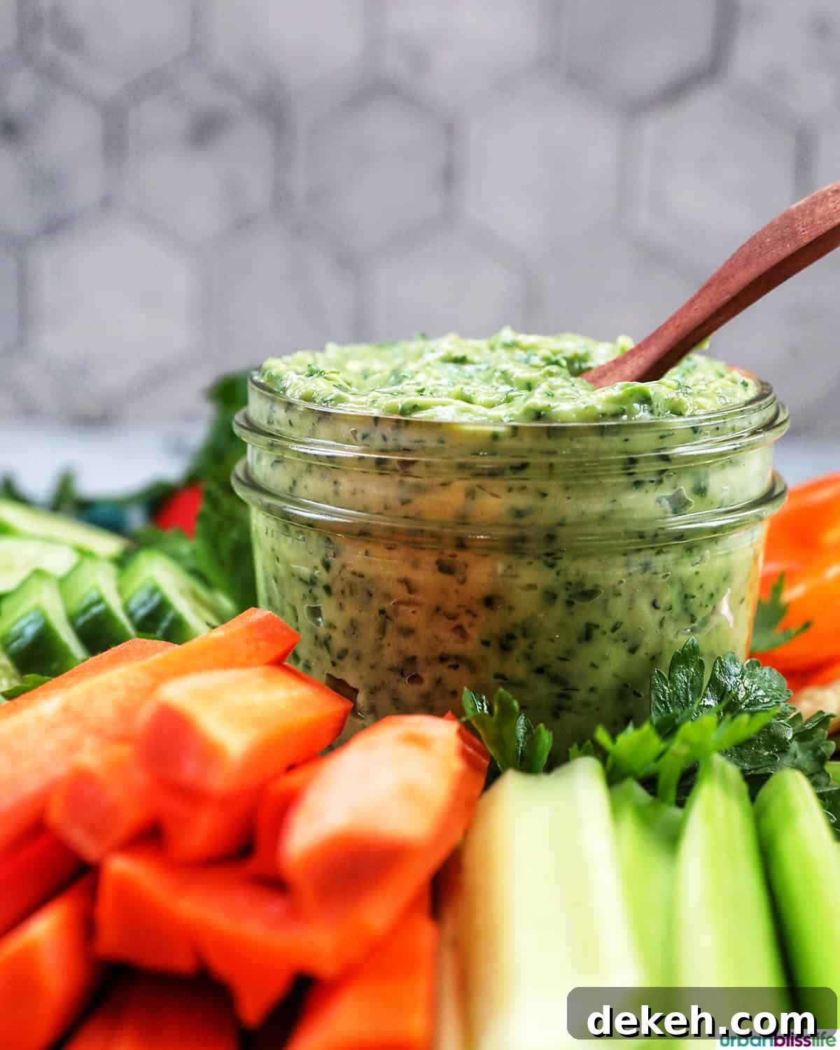 jar of vegan green goddess dressing in the center of sliced vegetables.