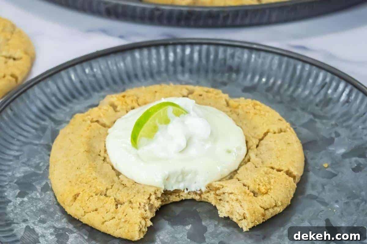 A large Copycat Crumbl Key Lime Cookies with a bite taken out, topped with white cream and a lime wedge, served on a gray plate.