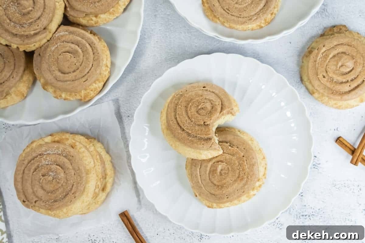Crumbl Copycat Churro Cookies are arranged on white plates and a napkin. One cookie on a plate has a bite taken out. Two cinnamon sticks are placed nearby on the white surface.