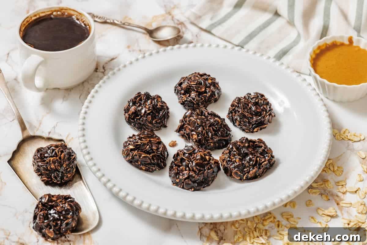 A white plate with seven Peanut Butter No-Bake Cookies on a marble surface, surrounded by a cup of coffee, a spoon, a bowl of nut butter, oats, and a striped cloth.