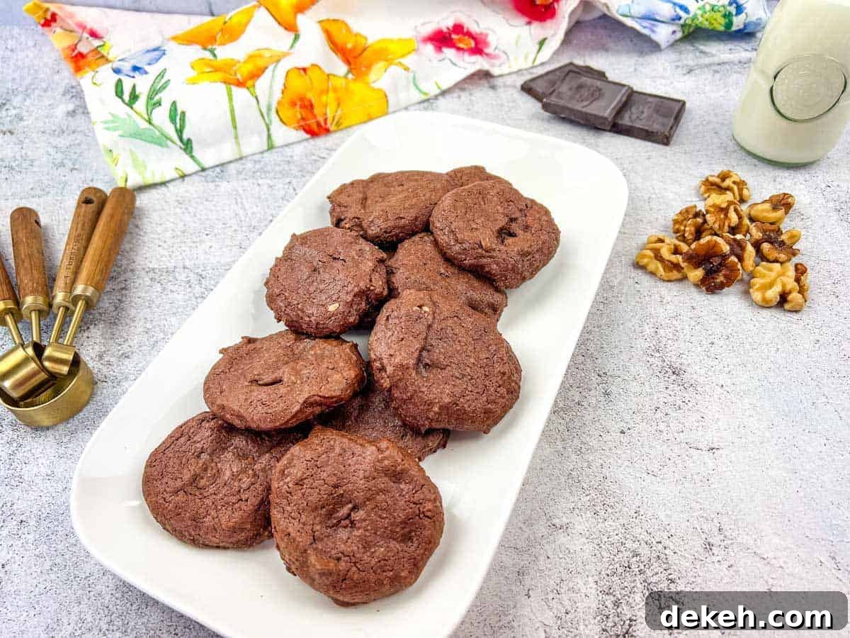 A plate of chocolate cookies with walnuts and chocolate pieces on the side.