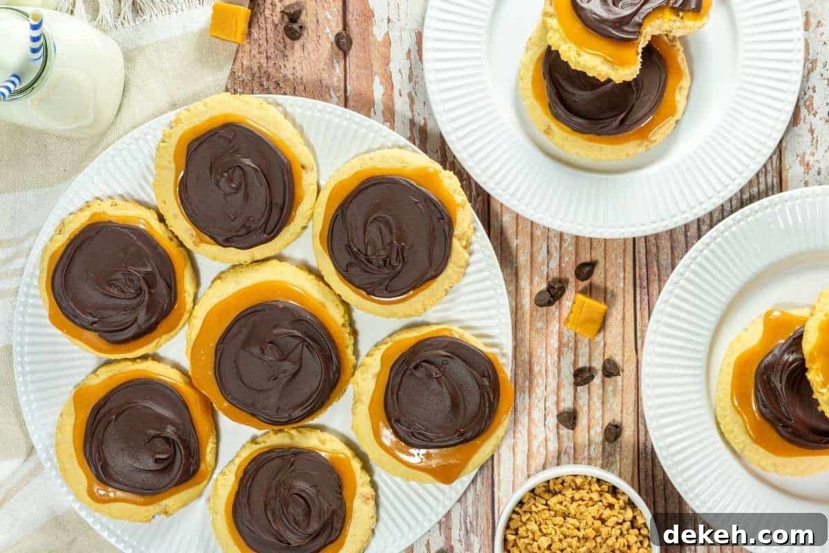 A plate of Copycat Crumbl Twix Cookies, with more cookies on separate plates, caramel pieces, and small chocolate chips nearby on a wooden table.