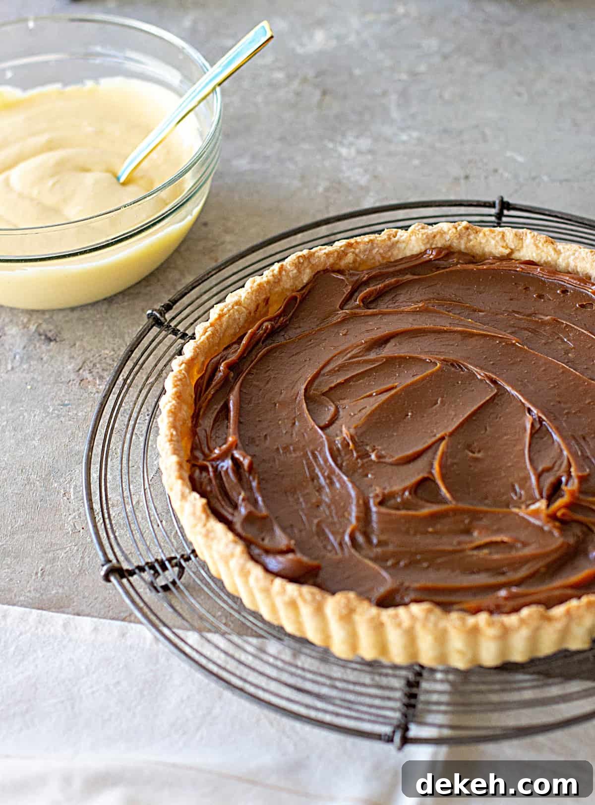 On a grey surface a wire rack with a pie tart dough with dulce de leche and bowl with lemon cream. 