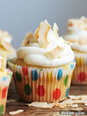 One central white frosted cupcake in dotted paper liner on wooden table with coconut flakes.