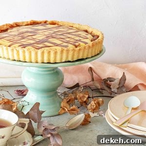 A lemon tart on a green cake stand. Stack of pink plates, dried leaves, a grey surface.