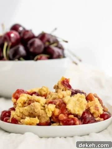 cherry dump cake on a white plate with a bowl of cherries behind