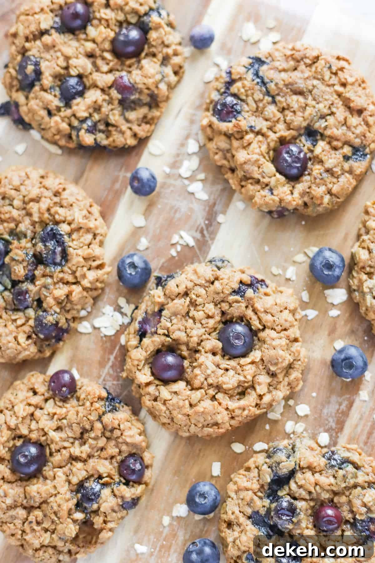 homemade blueberry oatmeal cookies on a wood cutting board with fresh blueberries and oats sprinkled throughout