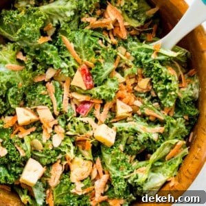 A wooden salad bowl filled with a kale apple salad with a serving spoon in it.