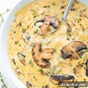 A bowl of vegan cream of mushroom soup with a spoon in it and topped with cooked mushrooms.