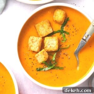 A bowl of butternut squash and red pepper soup garnished with croutons and fresh herbs.