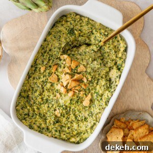 A white casserole dish filled with a vegan spinach artichoke dip with crushed crackers on top.