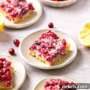 Cranberry lemon bars on plates with lemons and cranberries around them.
