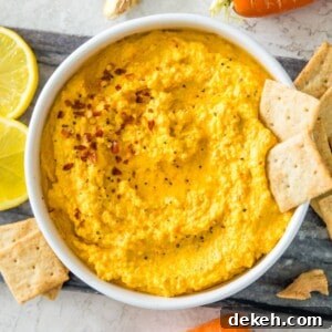 A bowl of carrot dip topped with chili flakes and two crackers.
