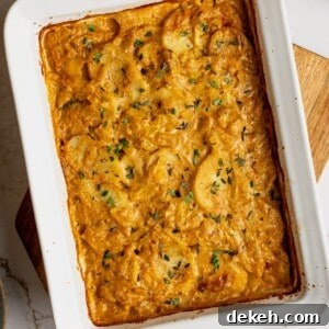 A pan filled with cooked scalloped potatoes garnished with fresh thyme.