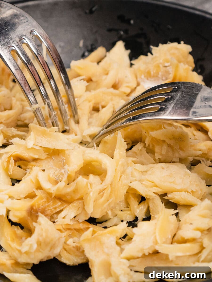 Breaking up saltfish with two forks in a black bowl