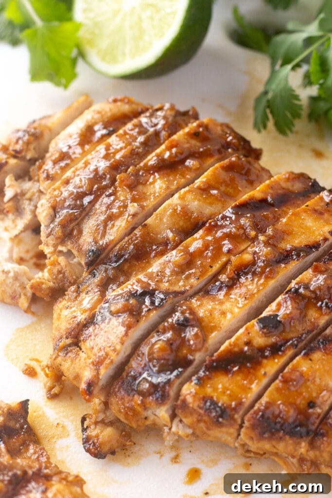 Close up of sliced grilled chicken breast on a white cutting board with lime and cilantro.