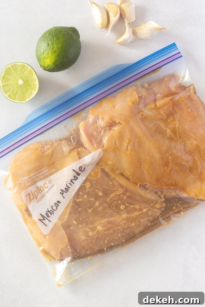 Top down shot of a ziploc bag with two flattened chicken breasts marinating in it. One and a half limes and five cloves of garlic are next to the bag.