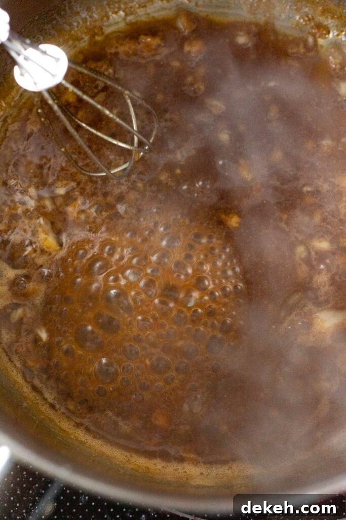 Close up of a brown marinade that's boiling in a small saucepan with a whisk stirring it.