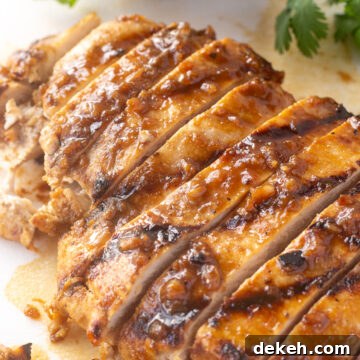 Close up of sliced grilled chicken breast on a white cutting board with lime and cilantro.