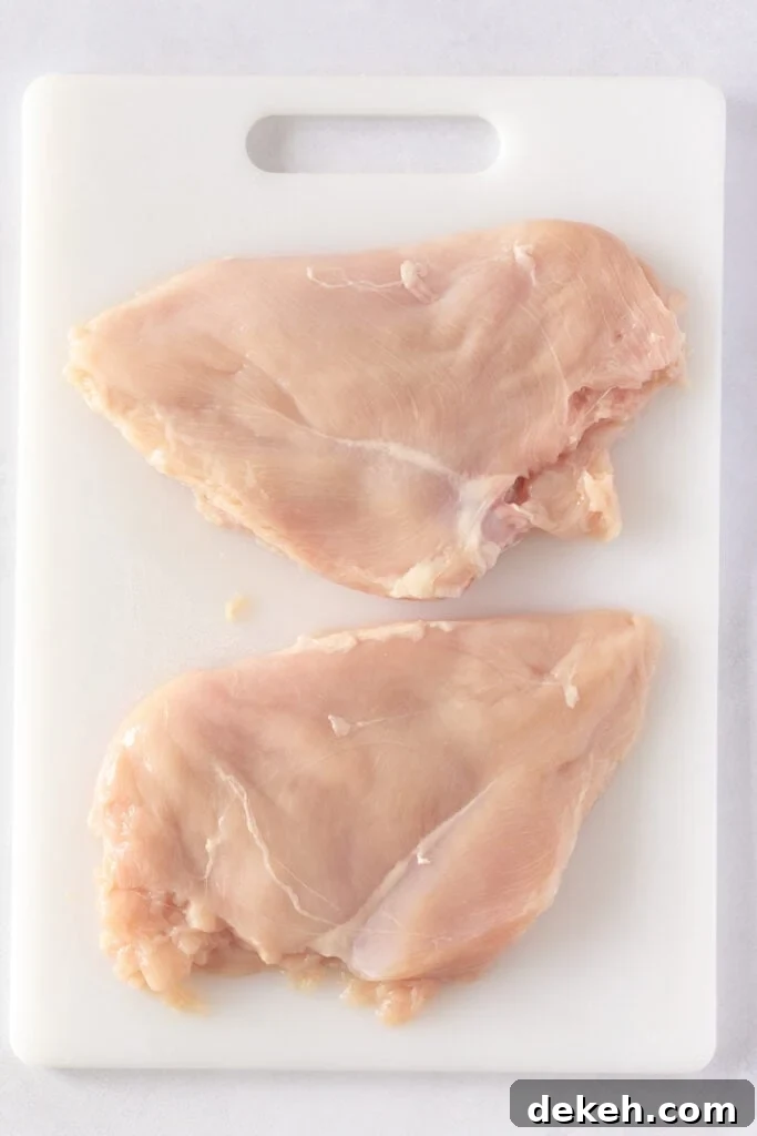 Two flattened chicken breasts on a white cutting board.