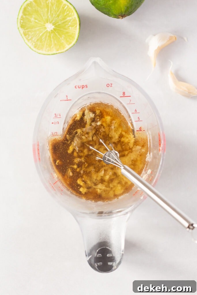 Top down shot of a brown marinade with garlic in it in a small measuring cup with a whisk sticking out.