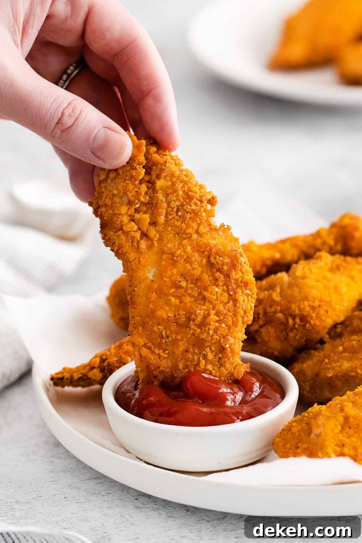 Hand dipping a chicken finger in ketchup.