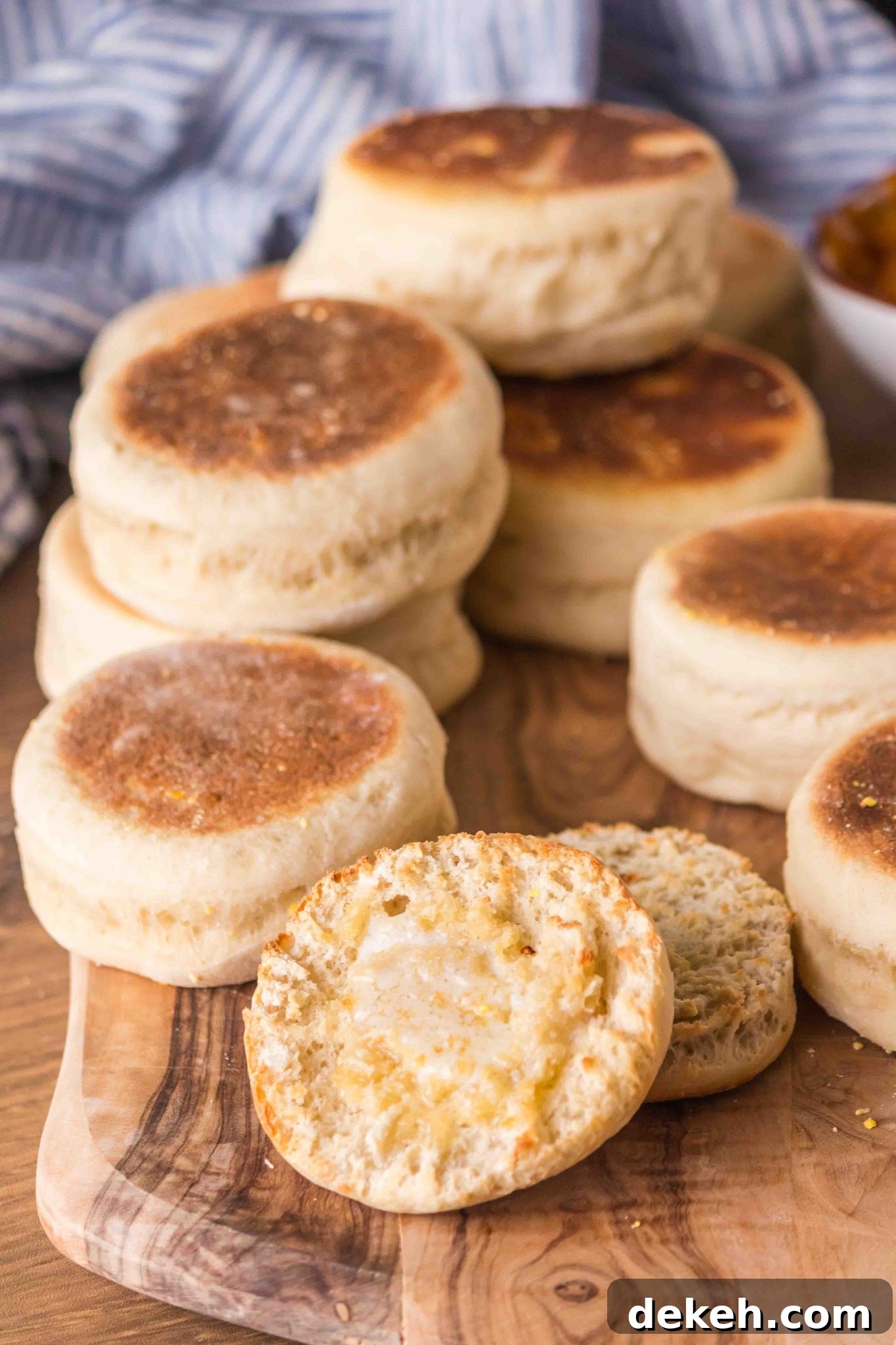 A wooden cutting board filled with baked English Muffins with a split one dripping with melted butter - Hostess At Heart