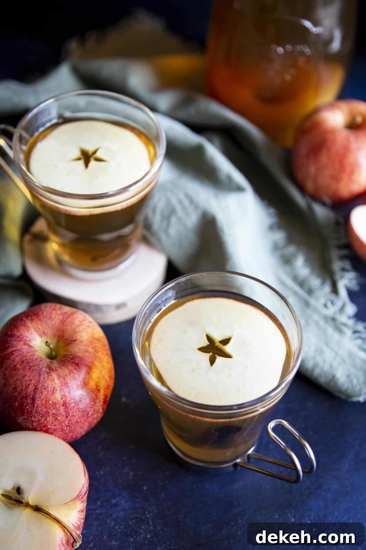 Hot apple cider in two glass mug garnished with apple slices.