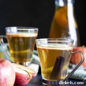 2 glasses of apple ciders next to some apple and a serving jug.