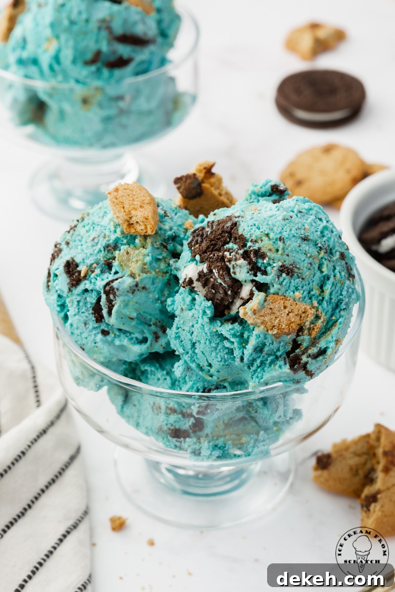 a footed glass ice cream dish filled with three scoops of blue ice cream filled with oreo and chocolate chip pieces